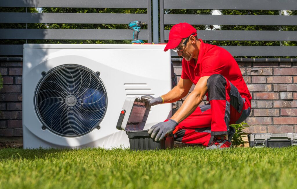 Professional technician performing maintenance on a heat pump system in Hialeah, FL, wearing a red uniform and gloves, with tools in a toolbox, ensuring efficient operation and reliability.