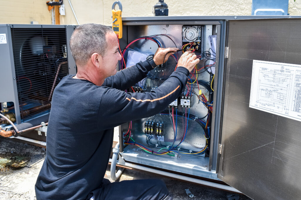 Technician repairing air conditioning unit, focusing on electrical components and wiring in Miami, showcasing emergency AC service expertise.