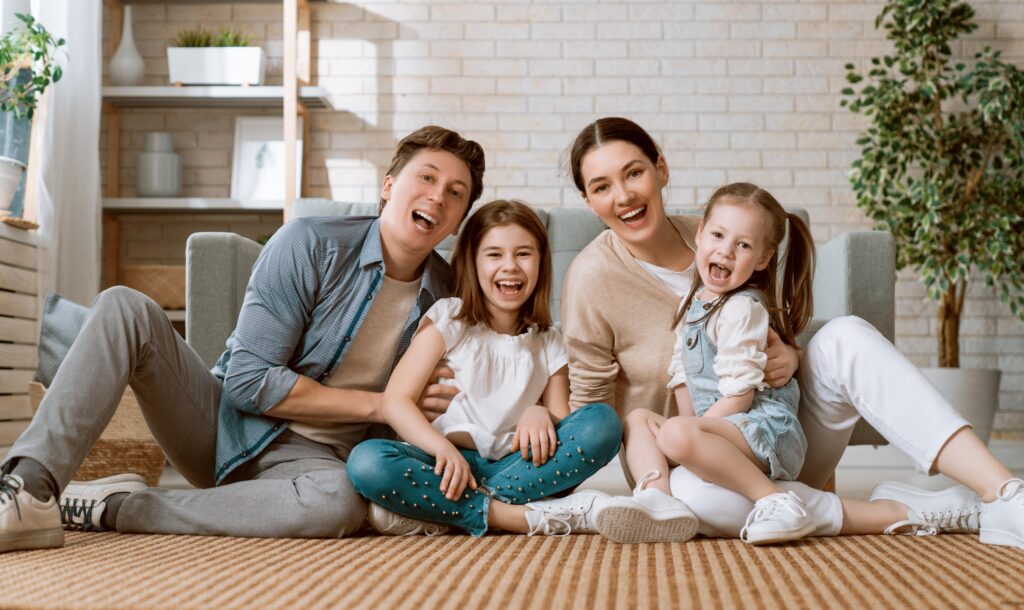Happy family of four smiling indoors. Indoor air quality impacts family's health and well-being.