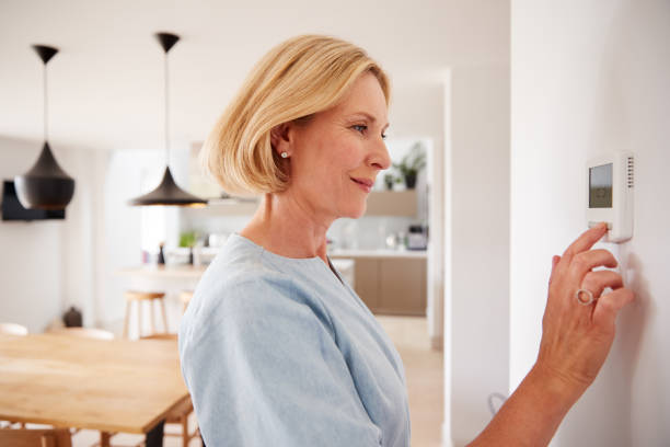 Woman adjusts a programmable thermostat in Miami, FL, for energy efficiency. Consider upgrading your home thermostat for better climate control.